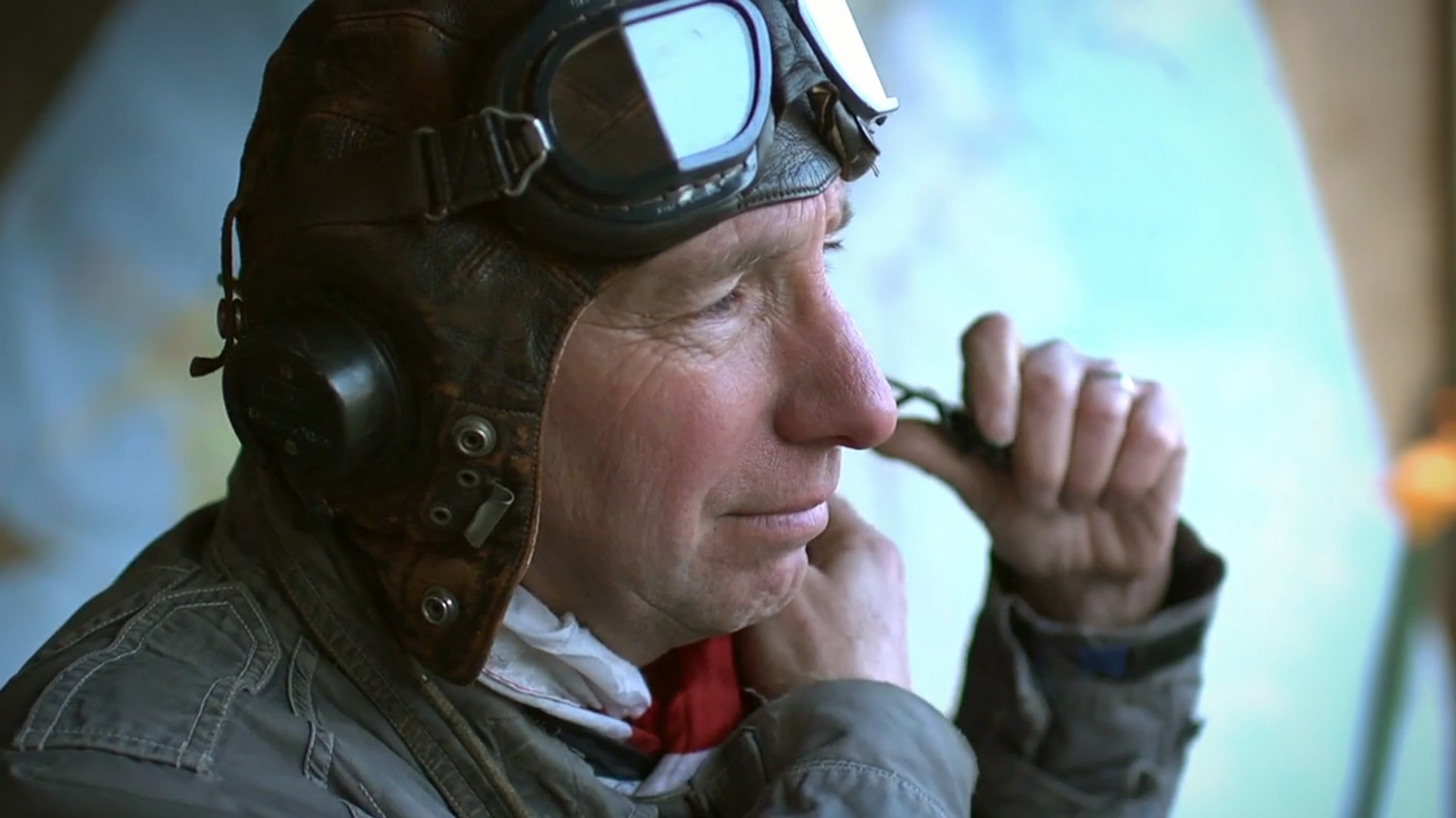 Alan James, a pilot strapping on his hat and flight goggles with a satisfied smile on his face.