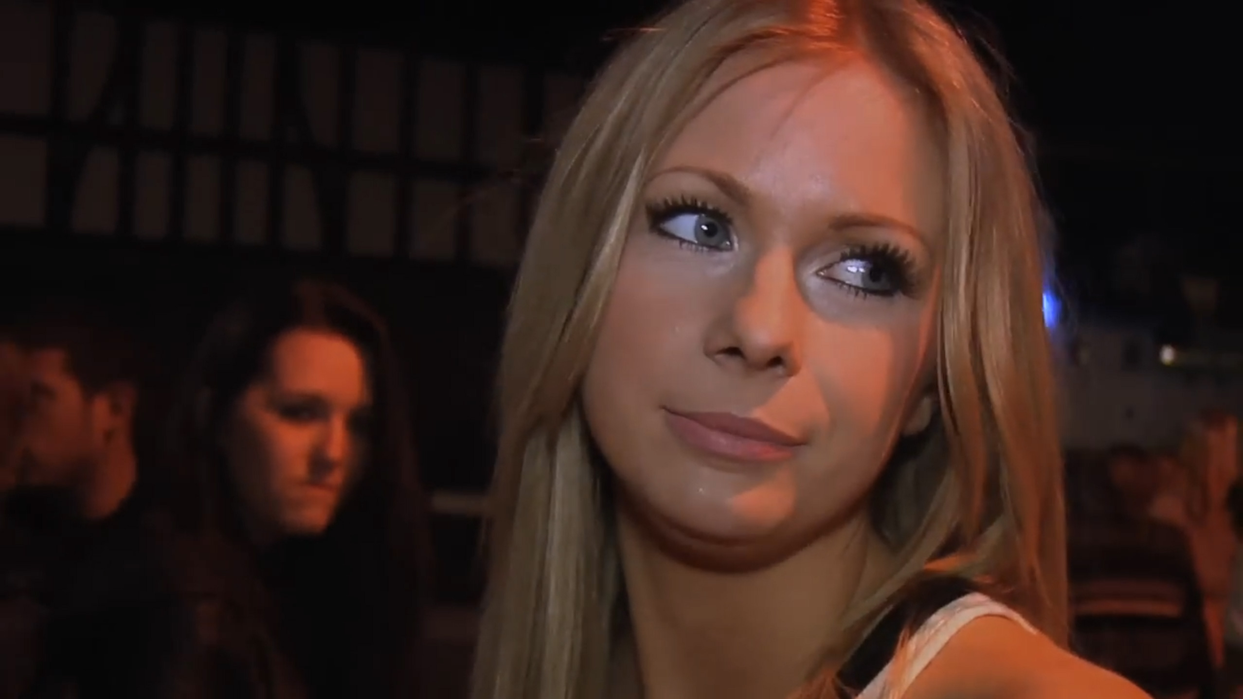 A woman looking upset while queueing for a club at night time.